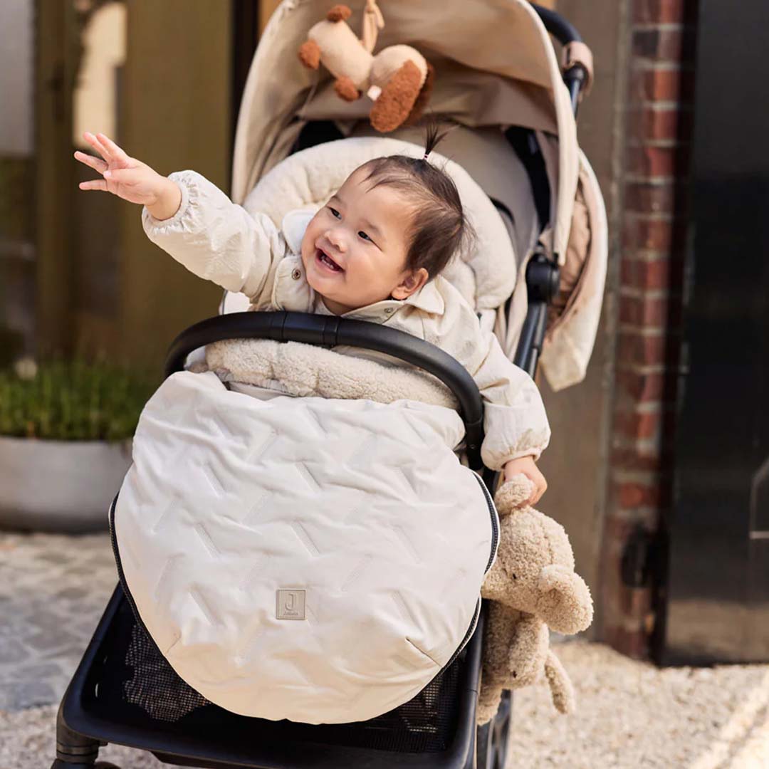 Een lachende baby zit in een kinderwagen met de Jollein wagenhanger op de achtergrond.
