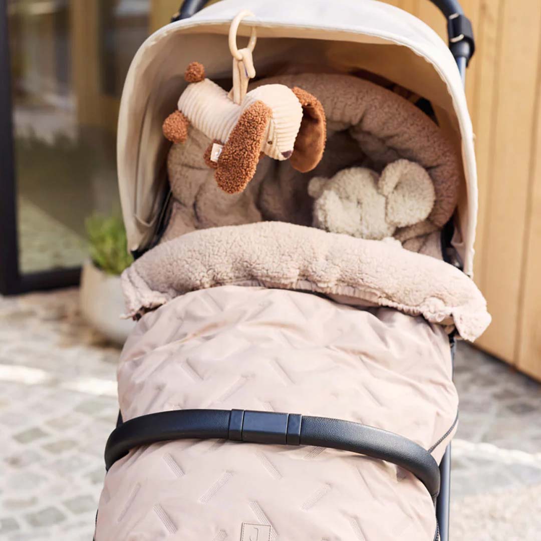 De Jollein wagenhanger in de vorm van een pluche hond hangt in een beige kinderwagen.