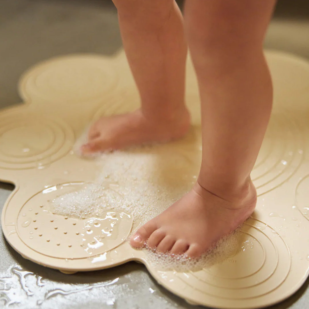 Blote babyvoetjes staan op de Jollein zandkleurige bloem badmat met water en bubbels.