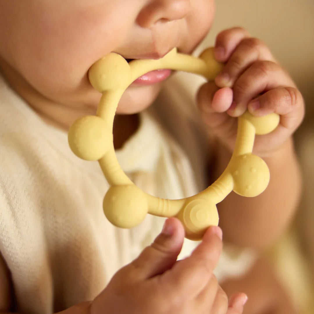 Een baby kauwt op de beige Jollein bijtring.