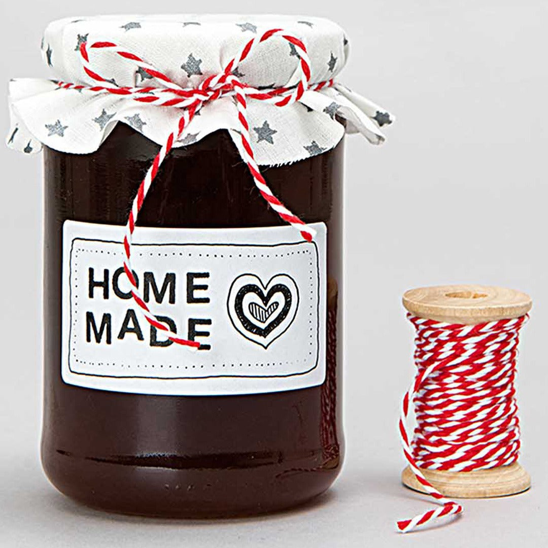 Een pot zelfgemaakte jam versierd met rood-wit gestreept katoengaren, met een klosje ernaast.