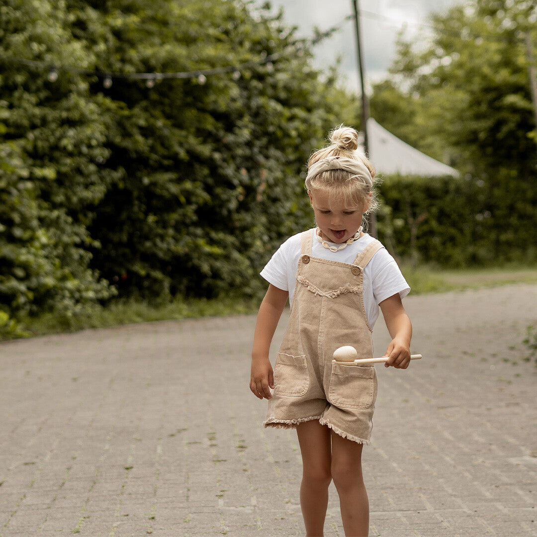 Een kind loopt buiten met het kids at work houten eierloop spel, balancerend met een ei op een lepel.