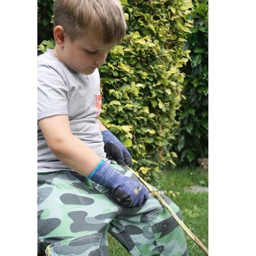 Een kind met handschoenen gebruikt het kids at work houtkrul schilmesje om een tak te bewerken.