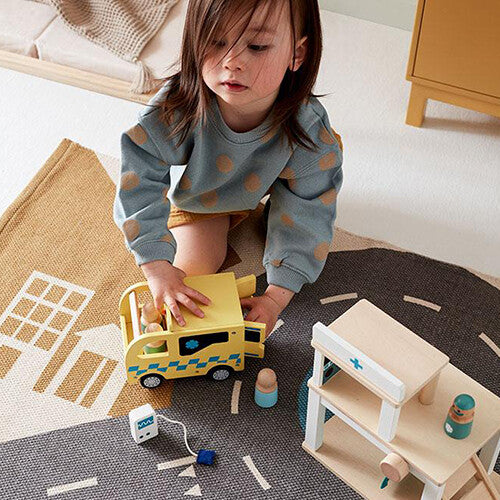 Een kind speelt op een speelkleed met de Kids Concept houten speelgoed ambulance en een houten ziekenhuis.