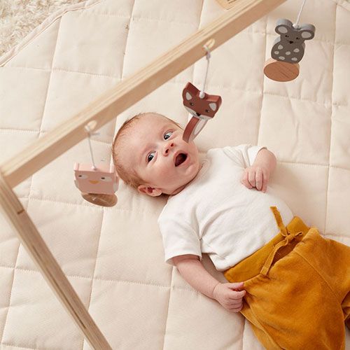 Baby ligt onder de Kids concept houten babygym en kijkt naar het hangspeelgoed met dieren.