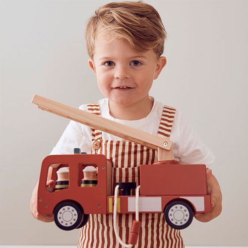 Een lachende peuter die de Kids Concept houten brandweerauto vasthoudt.