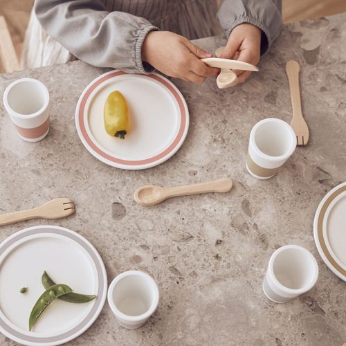 Bovenafzicht van kinderhanden die spelen met houten bestek en speelgoedservies op een marmeren tafel.