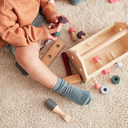 Een baby speelt op een tapijt met de kids concept houten gereedschapskist en kleurrijke houten gereedschappen.