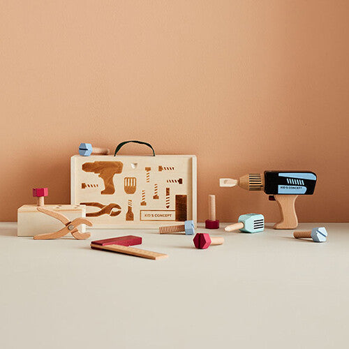 Kids Concept houten gereedschapskoffer en diverse houten gereedschapsstukken zoals een boor en tang liggen op een beige ondergrond.