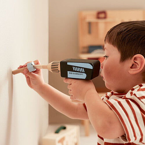 Een kind gebruikt de Kids Concept houten speelgoedboor om een schroef in een lichte muur te draaien.