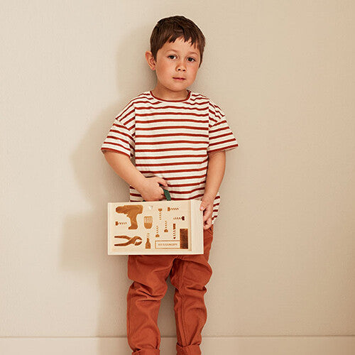 Een kind staat en houdt de Kids Concept houten gereedschapskoffer met gereedschapssilhouetten vast.