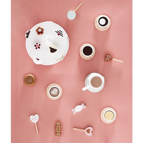 kids concept houten speelgoedkeuken accessoires, waaronder een theepot, kopjes en diverse snoepjes, op een roze achtergrond.