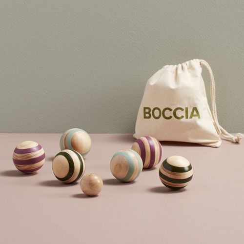 Kids Concept Boccia speelset met zes gestreepte houten ballen, een kleine houten bal en een katoenen zak op een roze ondergrond.