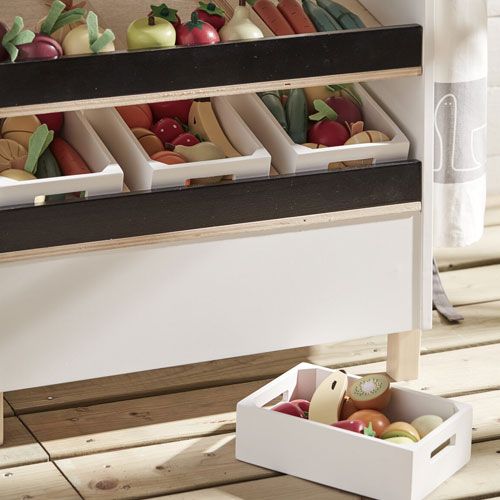 Kids Concept houten speelgoedgroenten en -fruit in witte kistjes op de planken van een speelgoedmarktstal.