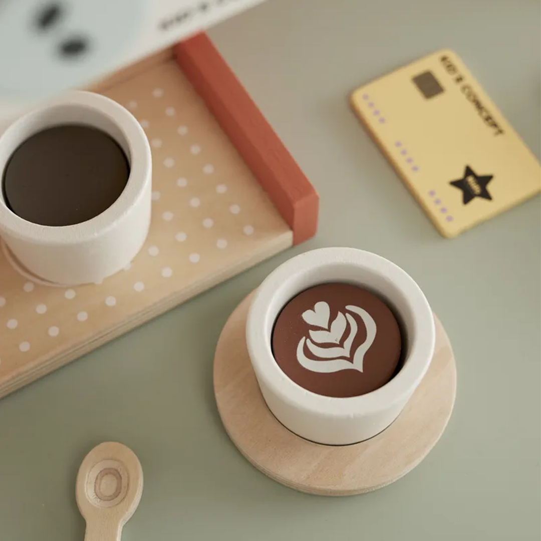 Detailopname van twee kopjes van de Kids Concept houten koffiemachine speelset, waarvan één met een latte art patroon, op houten schoteltjes.