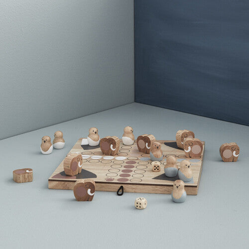 Kids Concept Ludo bordspel op een grijze ondergrond tegen een blauwe muur, met houten speelstukken en dobbelstenen.