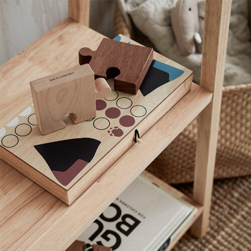 Het Kids Concept Ludo bordspel dichtgeklapt op een houten plank, met twee houten puzzelstukken erbovenop.