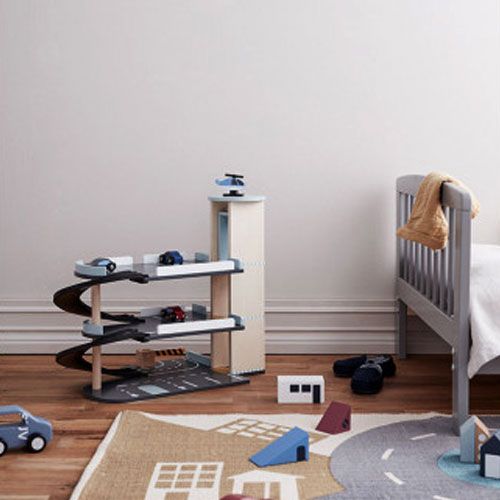 Kids Concept houten parkeergarage Aiden in een kinderkamer met een bed en een speelkleed met wegenpatroon.