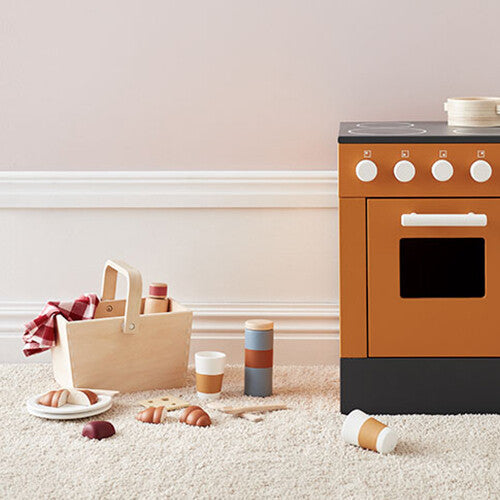 Kids Concept houten picknick speelset met mand en speelgoedeten naast een speelkeuken.