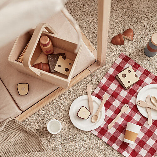 Bovenaanzicht van de houten picknick speelset met mand, rood geruite mat en speelgoedeten op een tapijt.