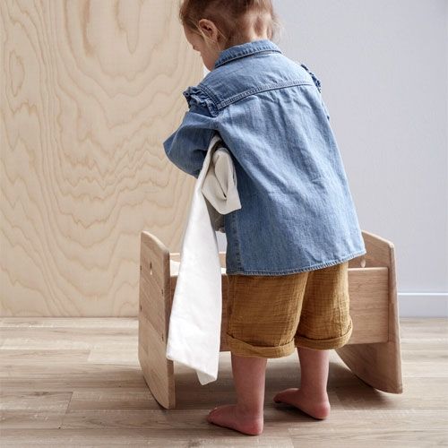 Een kind staat van achteren gezien naast de Kids Concept houten poppenwieg.