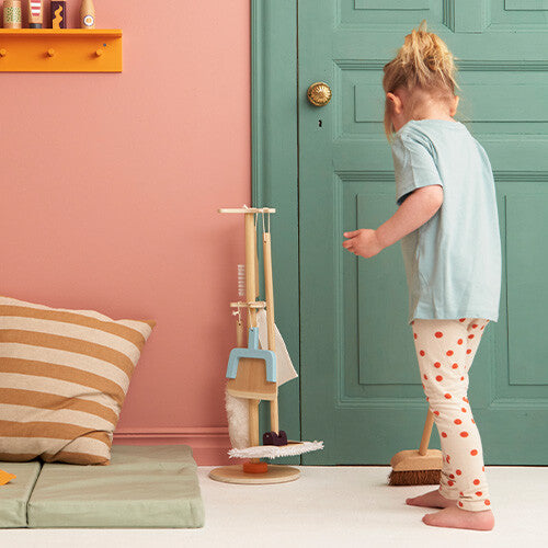 Een kind staat naast de Kids Concept houten schoonmaakset Kid's Hub en een bezem in een kamer.