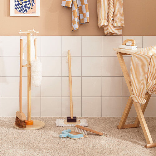 De Kids Concept houten schoonmaakset Kid's Hub met losse onderdelen ligt op een vloerkleed naast een strijkplank.