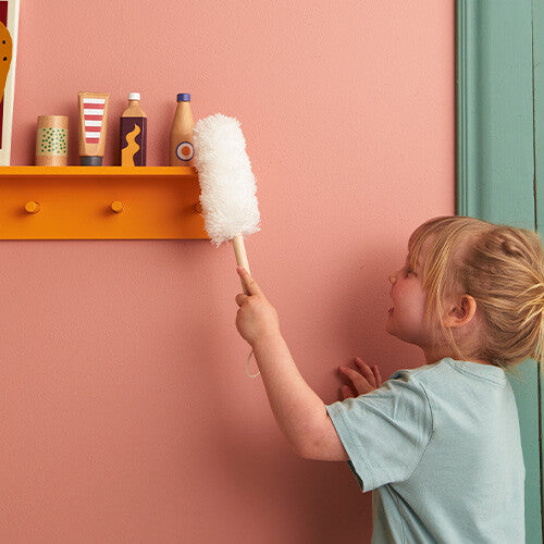 Een kind houdt de duster van de Kids Concept schoonmaakset omhoog tegen een roze muur.