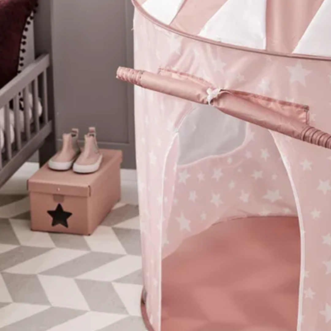 De roze speeltent met sterrenpatroon staat op een vloerkleed in een kinderkamer.