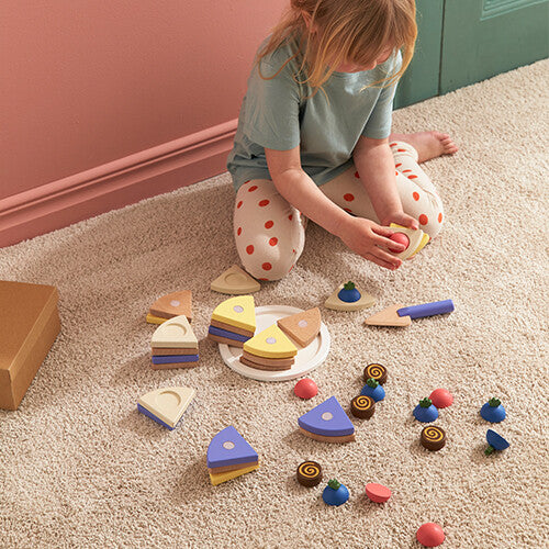 Een kind zit op de grond en speelt met de Kids Concept houten speelgoedtaart set, met alle stukken verspreid.