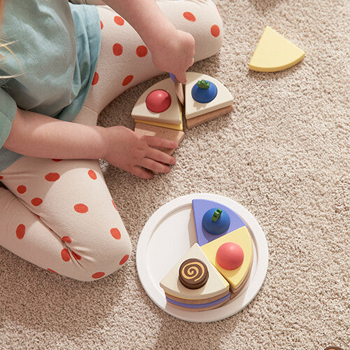 Een kind legt een stuk van de Kids Concept houten speelgoedtaart op een bord, met andere stukken ernaast.