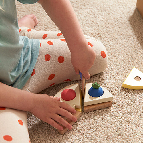 Een kind snijdt een stuk van de Kids Concept houten speelgoedtaart met de taartschep.