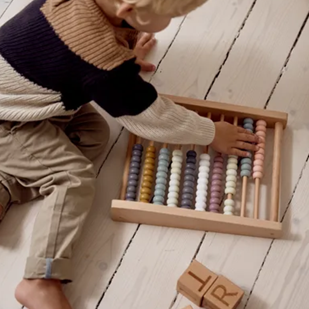 Een kind speelt op de grond met het Kids Concept houten telraam met veelkleurige kralen.