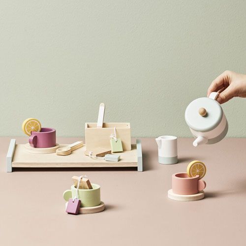 Een hand schenkt uit de Kids Concept houten theepot bistro in een kopje, met de complete theeset op een houten dienblad.