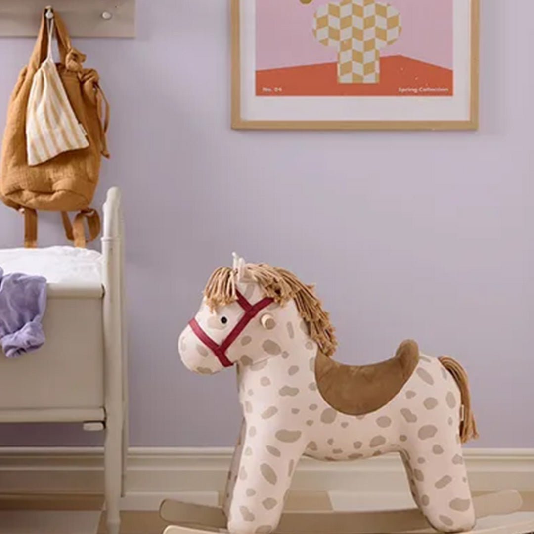 Kids Concept hobbelpaard met stippenpatroon in een kinderkamer naast een wit ledikant.