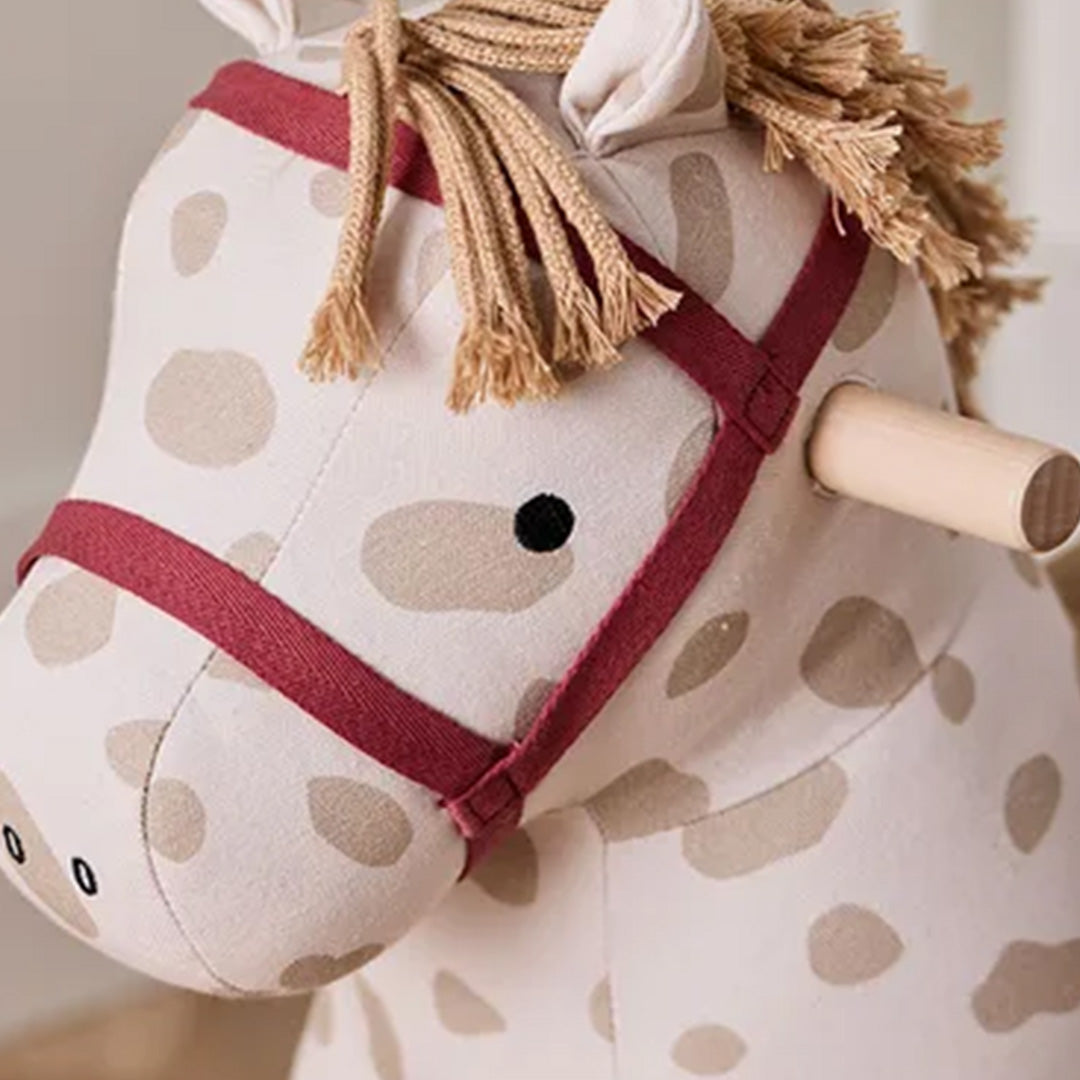 Detailopname van de kop van het Kids Concept hobbelpaard met beige stof met bruine stippen, rode teugels en houten handvat.