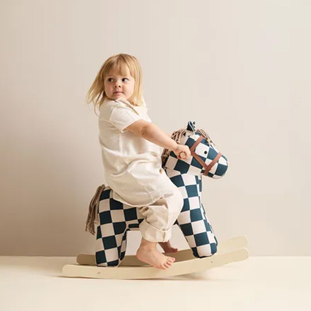 Een kind zit op het Kids Concept hobbelpaard met geruit patroon en kijkt over de schouder.