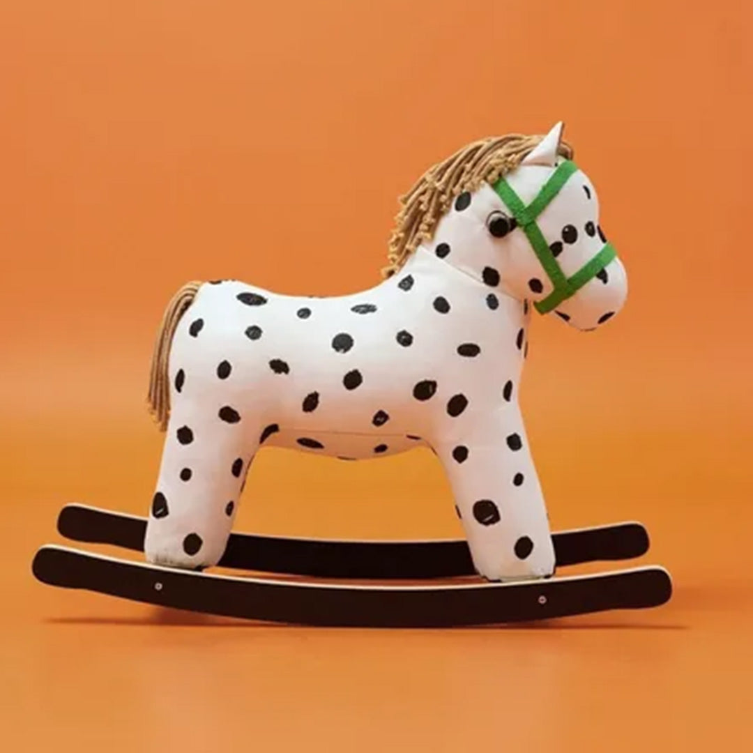 Kids Concept hobbelpaard Pippi, wit met zwarte stippen en groene hoofdstel, tegen een oranje achtergrond.