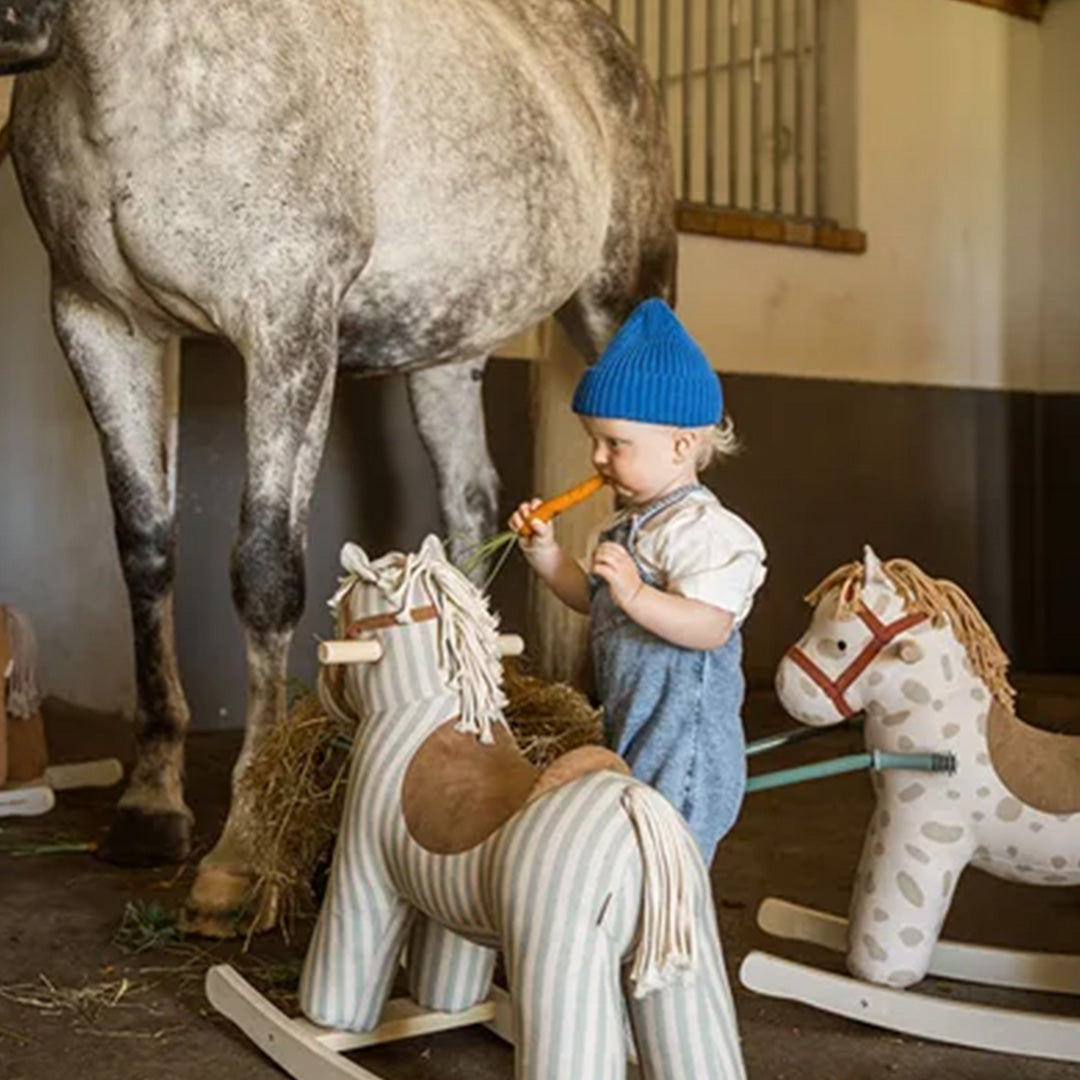 Een kind geeft een wortel aan een echt paard, met twee Kids Concept hobbelpaarden op de voorgrond.