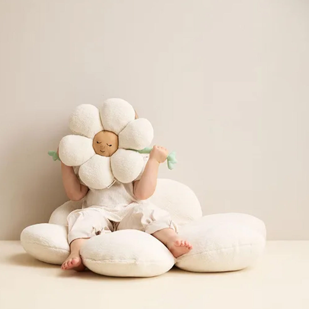 Een kind zit op een bloemkussen en houdt een kids concept bloemkussen met slapend gezicht voor haar hoofd.