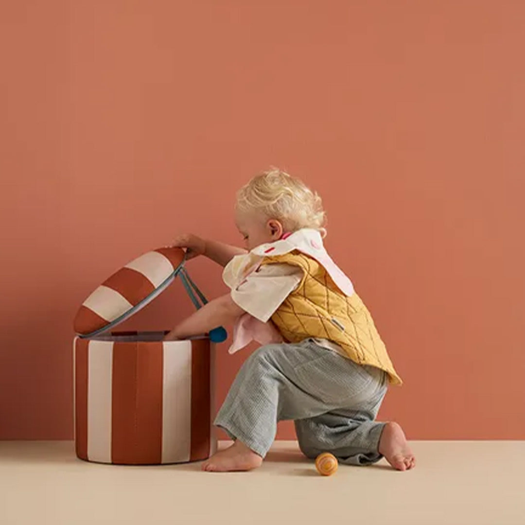 Een kind opent de kids concept gestreepte opbergpoef om speelgoed erin te doen.