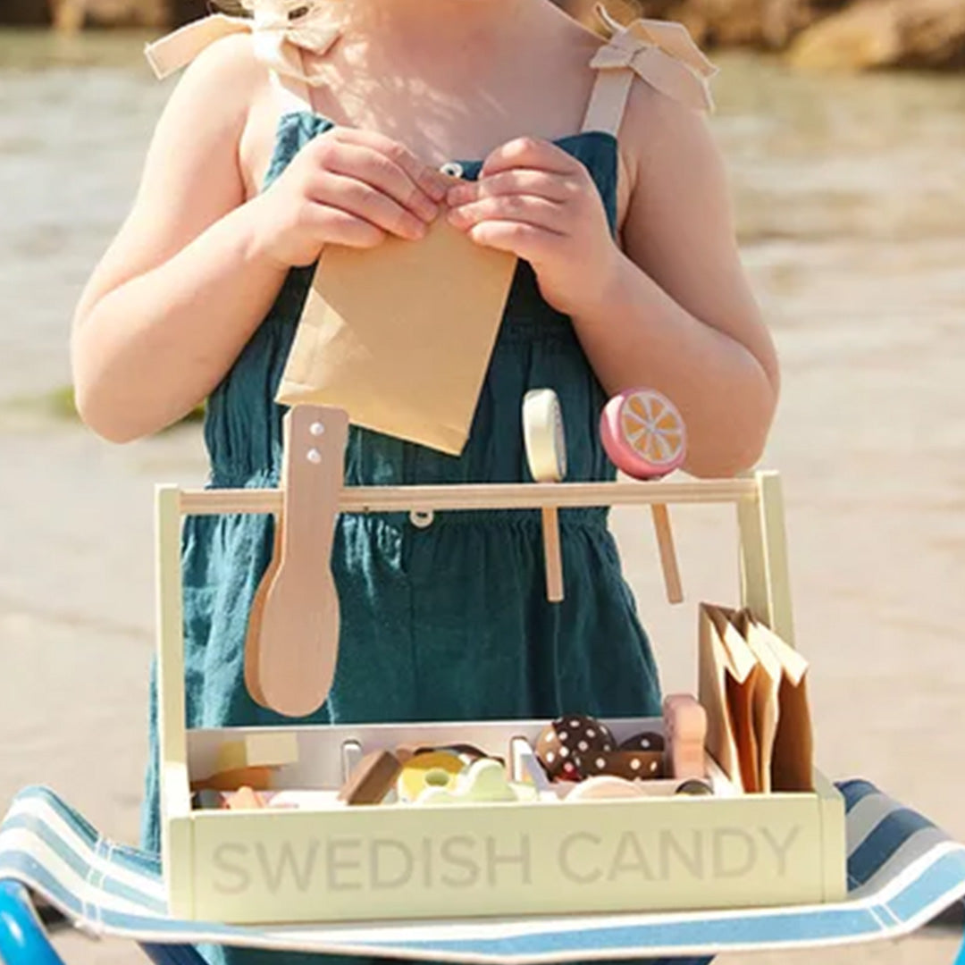 Een kind staat achter de Kids Concept houten snoepwinkel speelset en houdt een papieren zakje vast.