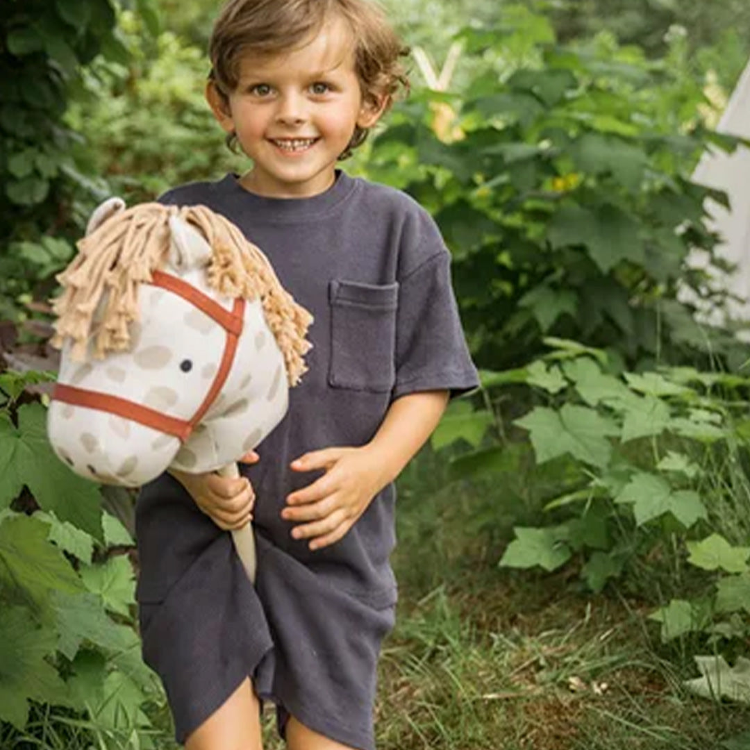 Een lachend kind speelt buiten met het Kids Concept stokpaard Dotty.