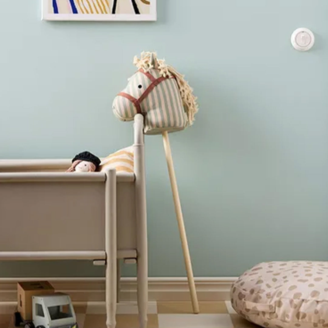 Gestreept stokpaard leunt tegen een lichtblauwe muur naast een wieg in een kinderkamer.