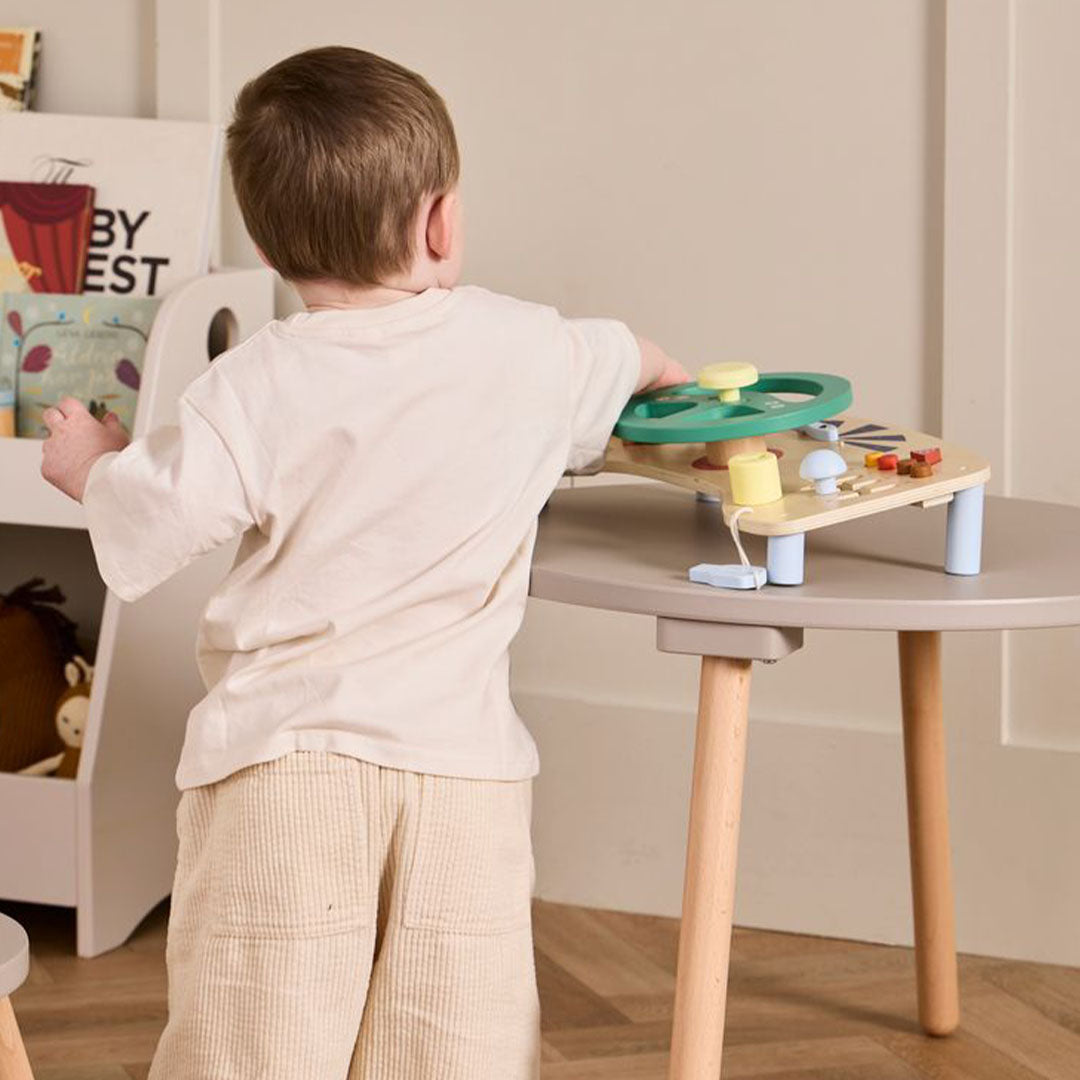 Een kind staat achter een grijze tafel en speelt met het Kids Concept houten activiteitenpaneel auto.