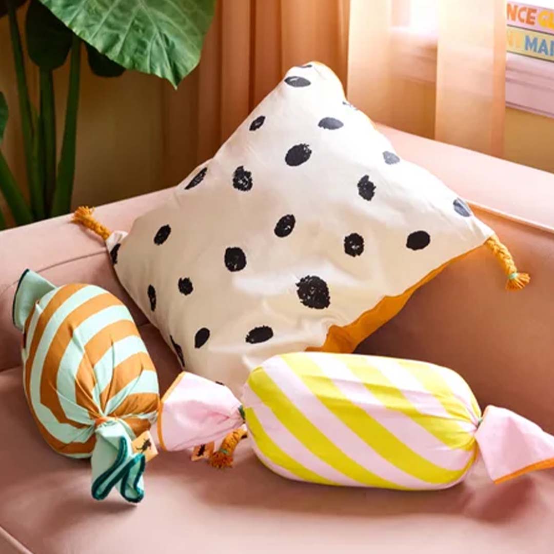 Twee Kids Concept snoepkussens en een vierkant kussen met stippen op een roze bank.