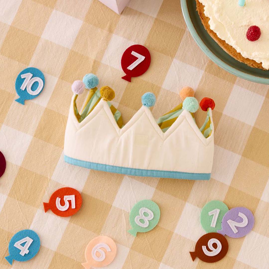 Kids Concept verjaardagskroon met cijfer 7 op een geruite tafel, omringd door losse cijferballonnen en een stuk taart.