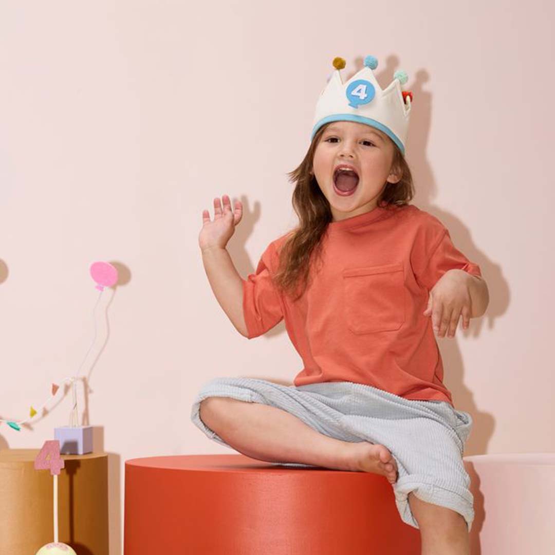 Een blij kind draagt de Kids Concept verjaardagskroon met het cijfer 4 op een oranje blok.