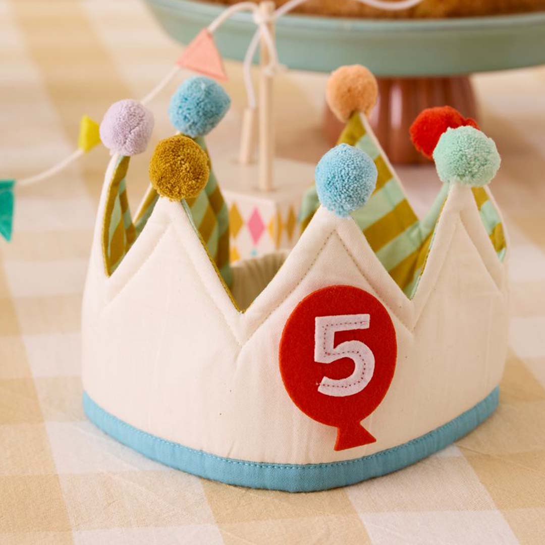 Kids Concept verjaardagskroon met kleurrijke pompons en een rode ballon met het cijfer 5, liggend op een geruite ondergrond.