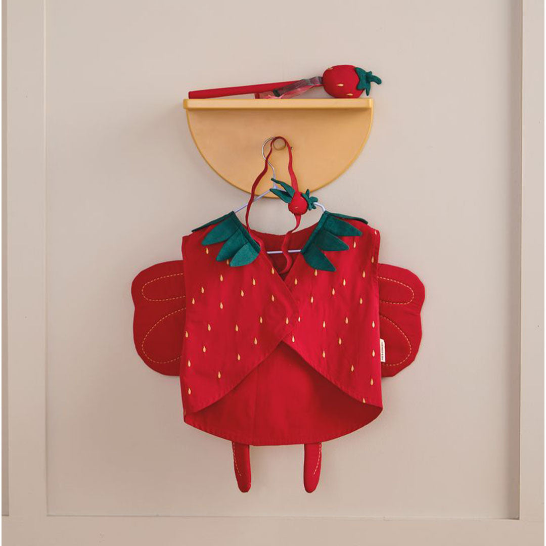 De Kids Concept aardbeienfee verkleedkleding set hangt aan een haakje aan de muur, met het vest, de vleugels, hoofdband en toverstaf.
